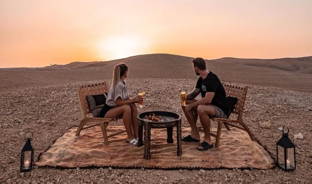 Sunset aperitif overlooking Agafay Desert with golden sand dunes and vibrant sky
